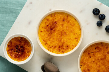 Creme brulee. Traditional French vanilla cream dessert. Burned cream, burnt or Trinity creme. Spanish crema catalana, four ramekin on marble. Vertical, top view
