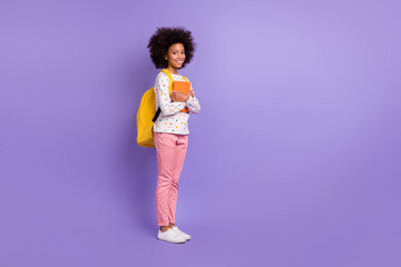 Full length profile side photo of little dark skin girl hold book wear bag pink pants school isolated on violet color background