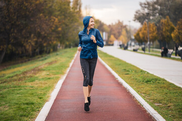 Beautiful adult woman is jogging outdoor on cloudy day in autumn.