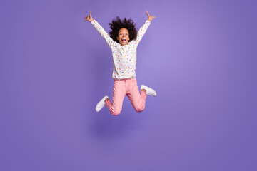 Full body little dark skin funky girl jump raise hands wear casual clothes isolated on purple color...