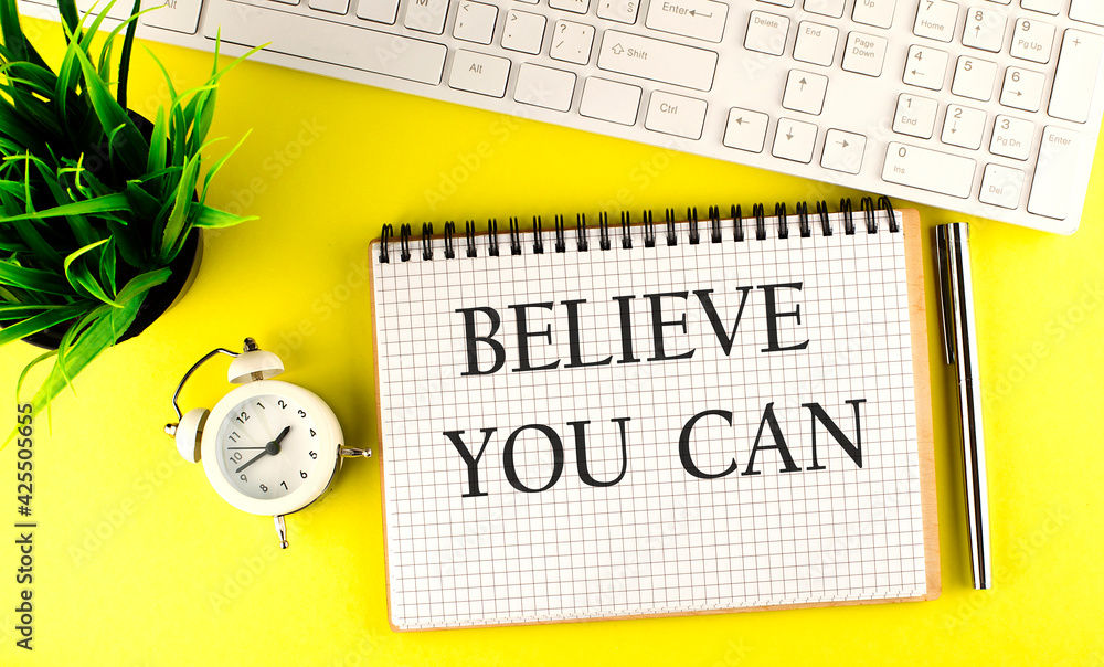 Poster believe you can text on notebook with keyboard , pen and alarm clock on the yellow background