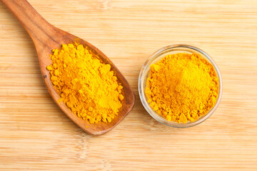Turmeric powder in wooden spoon and glass bowl on white background.