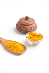 Turmeric powder in wooden spoon and glass bowl on white background.