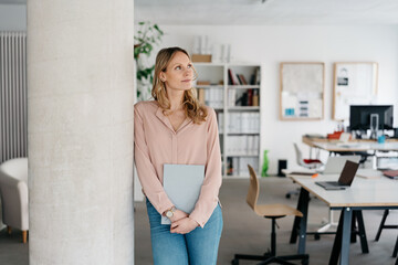 Thoughtful young businesswoman standing daydreaming in a spacious office