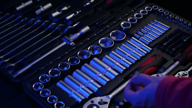 male worker in red clothes using chrome vanadium tools connecting socket and head from wrench in auto shop in blue light