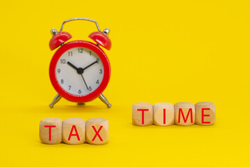 The word tax time written on wooden cubes with an alarm clock on yellow background. Tax payment reminder and annual taxation concept.