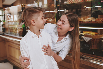 Happy beautiful woman smiling at her lovely son while shopping together for pastry at bread store