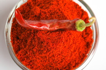 Dried red chilli and powder in glass bowl on white background.