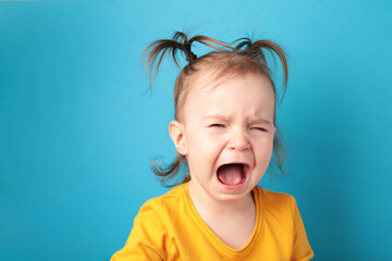 Upset little baby girl crying on blue background. Top view