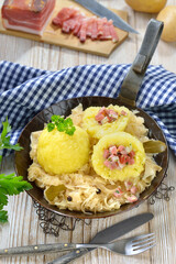 Mit Südtiroler Speck gefüllte Kartoffelknödel auf Sauerkraut im Eisenpfandl serviert  - ...