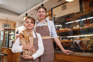 Lovely young boy helping his mother selling bread at their family bakery, copy space