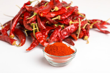 Dried red chilli and powder in glass bowl on white background.