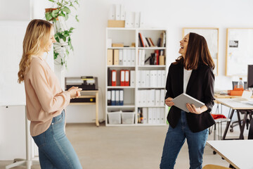 Two businesswoman standing laughing together happily in an office