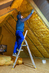 The man insulates the attic of the house with mineral wool