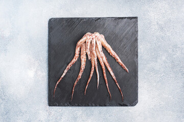 Raw squid tentacles on a black slate board. copy space Top view. Grey background.
