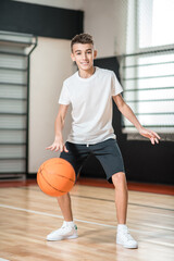 Fototapeta premium Teen in white tshirt playing basketball in the gym and looking involved