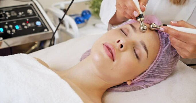 Beautiful woman receiving facial microcurrent treatment at spa salon. Beautician using electrical impulses for facial procedures. Woman in spa salon. Woman in a spa salon on cosmetic procedures. 