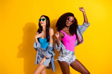 Photo of two crazy funny ladies carefree dance wear sunglass singlet jeans outfit isolated yellow color background