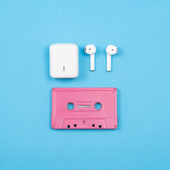 pink audio cassette with white wireless headphones on a blue background. stock photo