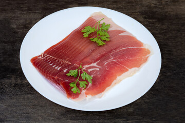 Thin slices of jamon with parsley twigs on white dish