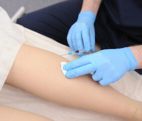 The doctor injects a syringe under the knee. A doctor makes an injection to the varicose veins on a woman s leg, close-up, sclerotherapy, stripping, phlebeurysm, medical.
