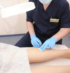 The doctor injects a syringe under the knee. A doctor makes an injection to the varicose veins on a woman s leg, close-up, sclerotherapy, stripping, phlebeurysm, medical.
