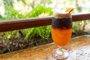 A glass of iced americano black coffee with orange juice topping with sliced orange on green nature background