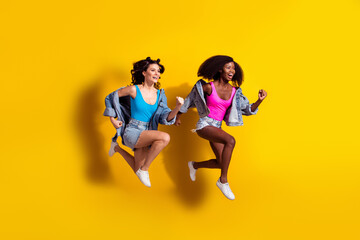Fototapeta na wymiar Photo of two pretty adorable young ladies wear jeans outfit jumping running fast isolated yellow color background