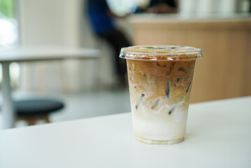Iced coffee latte. A plastic cup of espresso coffee shot with milk on white table. (front view)
