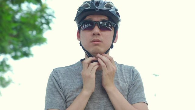 Asian male athlete put on helmet before start riding bicycle in park.