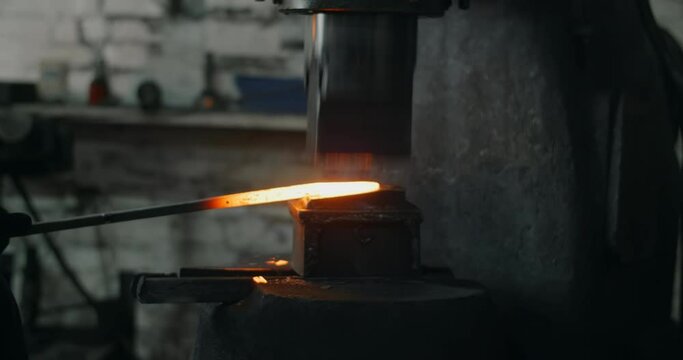 Blacksmith uses a hydraulic hammer to forge hot metal in his workshop, automatic hammer is shaping the red-hot metal, blacksmith craft, forged metal, 4k 60p Prores HQ