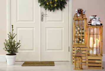 Beautiful Christmas lanterns and fir tree near entrance indoors