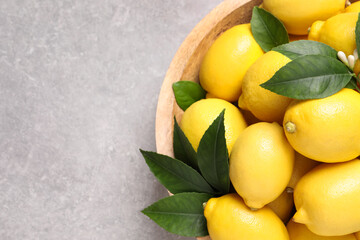 Many fresh ripe lemons with green leaves on light grey table, top view. Space for text