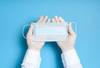 hands in medical gloves with a medical breathing mask on a blue background, health care prevention...