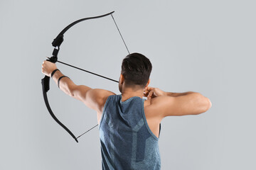 Man with bow and arrow practicing archery on light grey background, back view