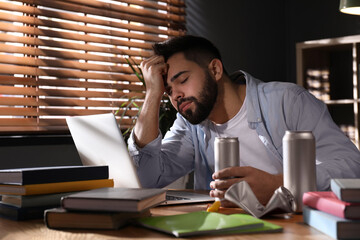 Tired young man with energy drink studying at home