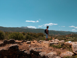 tourist looks at the mountains while standing above the ruins of the nuraghi - sardinia
