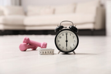 Alarm clock, measuring tape and dumbbells on wooden floor indoors. Morning exercise