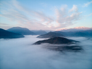 Aerial view, sea of fog and clouds illuminated by the rising sun, snow on the tops of the mountains. Russia