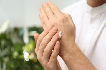 Man applying moisturizing cream onto hand on blurred background, closeup