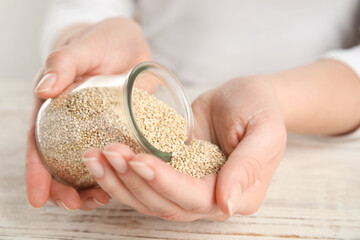 Woman with jar of white quinoa at wooden table, closeup