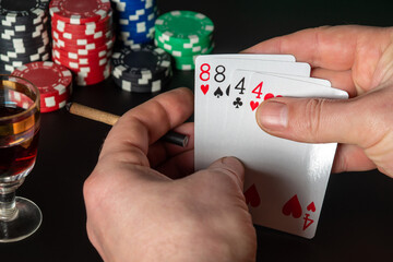 Poker cards two pairs combination. Close up of a gambler hand is holding playing cards and sigar in poker club