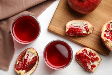 Glasses of pomegranate juice and fresh fruits on white wooden table, flat lay