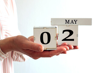Calendar for May 2: cubes with the numbers 0 and 2, the name of the month in English in the hands of a young woman on a gray background, side view