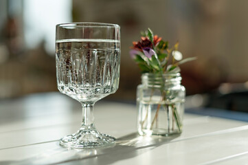 glass of mineral water and small bouquet of flowers in jar on table in sunlight, abstract, healthy...