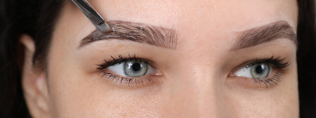 Beautician applying tint during eyebrows correction procedure on light grey background, closeup