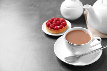 Delicious tea with milk in white cup near dessert on grey table. Space for text
