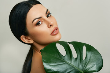 Skin care. Mixed race woman with fresh healthy skin holding monstera leaf near her face © Peakstock