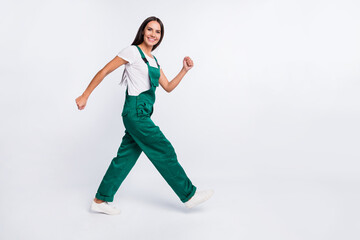 Photo of cheerful worker lady walk look camera wear green overall footwear isolated white color...
