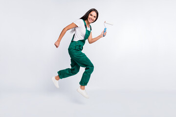 Photo of crazy pretty lady jump go hold roller look camera wear green overall shoes isolated white...
